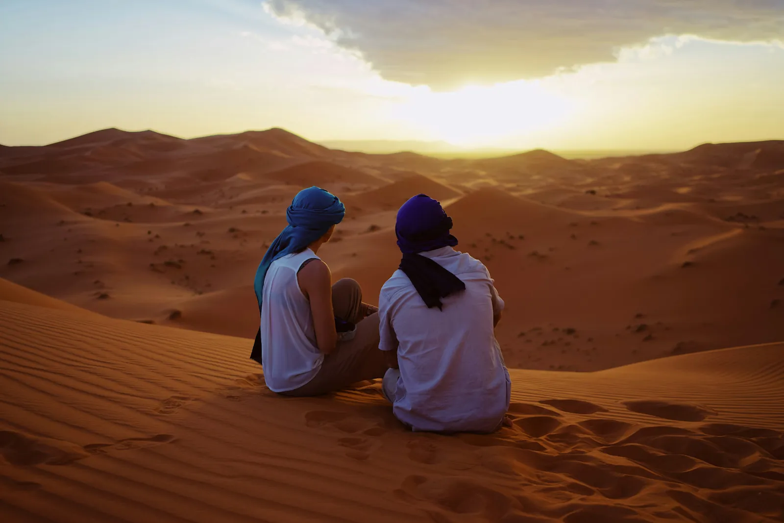 Dos viajeros con turbante sentados en una duna del Sahara al atardecer